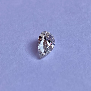 May include: A clear pear-shaped diamond gemstone on a white background.