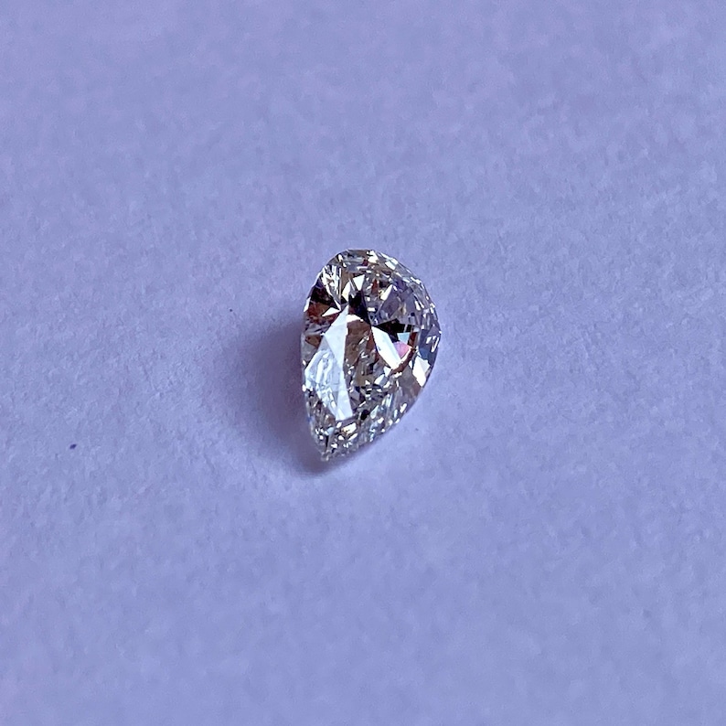 May include: A clear pear-shaped diamond gemstone on a white background.