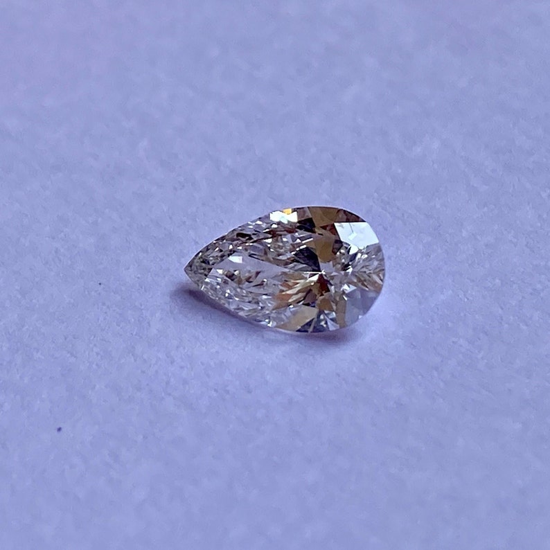 May include: A pear-shaped diamond gemstone with a clear, brilliant cut. The diamond is set on a white background.