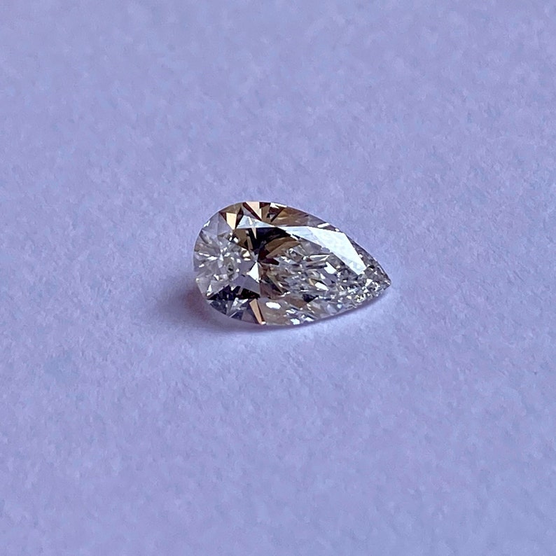 May include: A pear-shaped diamond gemstone with a clear, faceted surface.