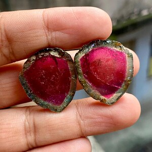 Pu&ograve; includere: Due cabochon di pietra preziosa rosa, verde e nera. I cabochon sono a forma di cuore e hanno una superficie liscia e lucida.