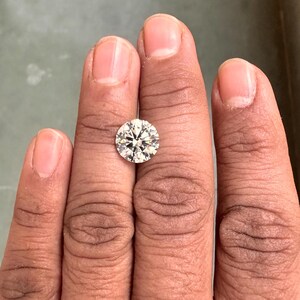 May include: A clear round diamond gemstone on a finger.