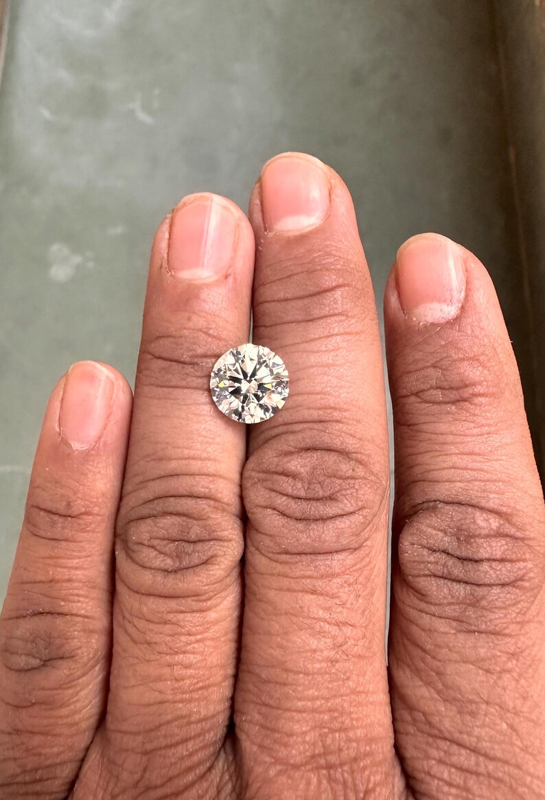 May include: A clear round diamond gemstone on a finger.