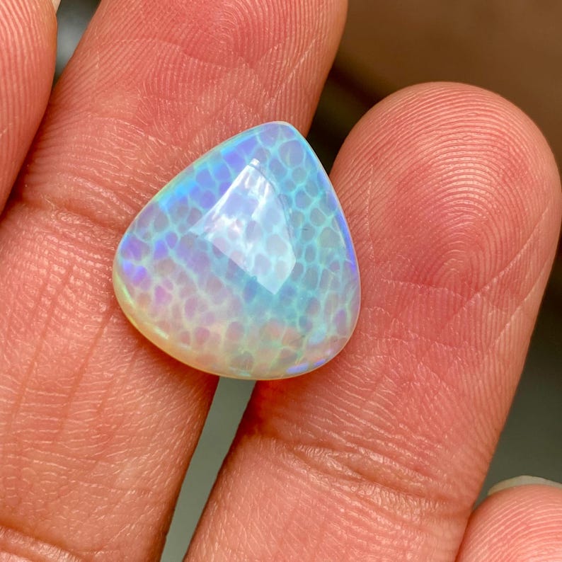 May include: A triangular, iridescent opal cabochon with a white base and blue, green, and purple flashes. The opal has a textured surface.
