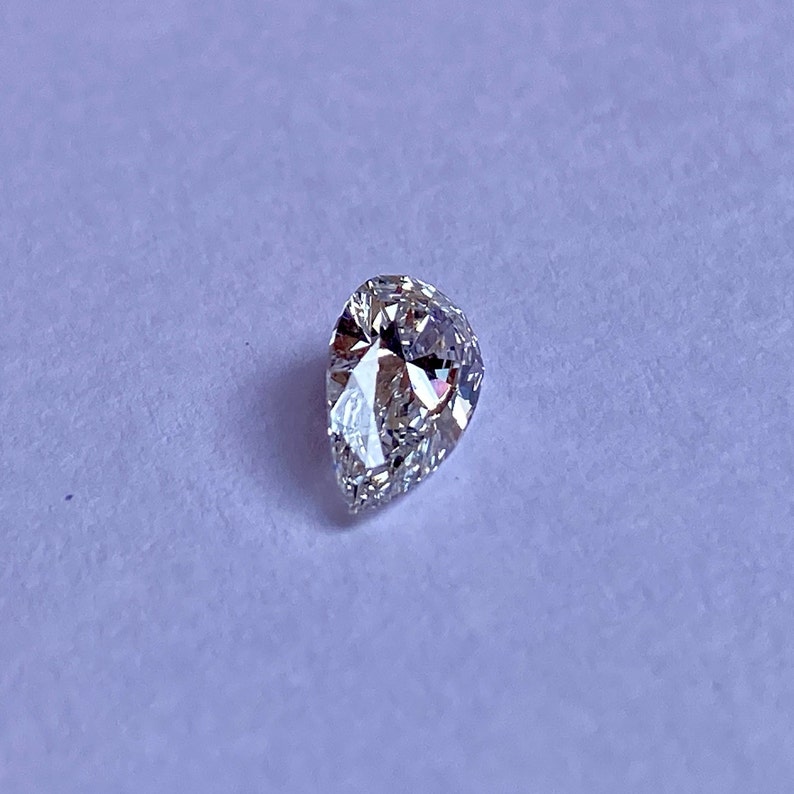 May include: A pear-shaped clear diamond gemstone on a white background.