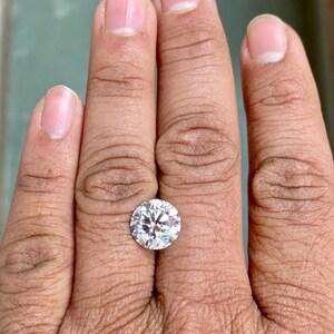 May include: A clear round diamond gemstone on a finger.