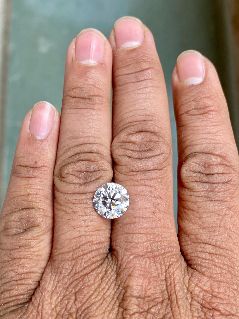 May include: A clear round diamond gemstone on a finger.