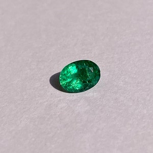 May include: A vibrant green emerald gemstone with a faceted oval shape.