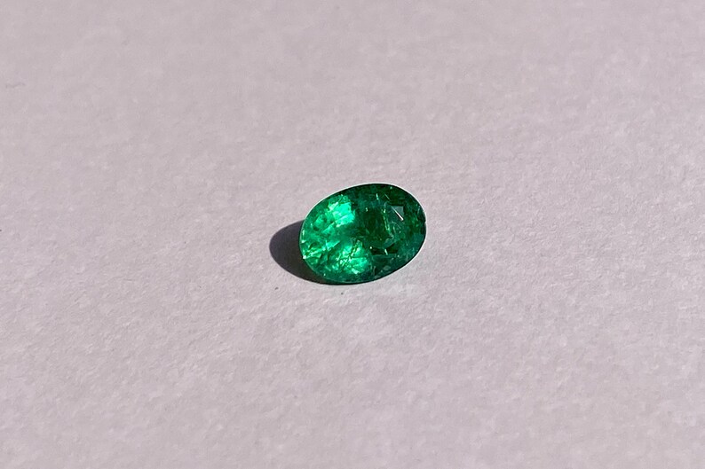 May include: A vibrant green emerald gemstone with a faceted oval shape.