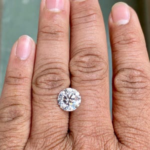 May include: A clear round gemstone on a finger, the gemstone is set in a ring.