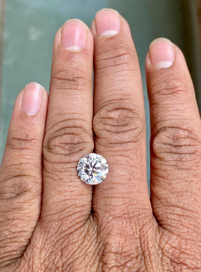 May include: A clear round gemstone on a finger, the gemstone is set in a ring.