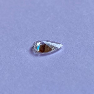 May include: A clear pear-shaped diamond gemstone on a white background.