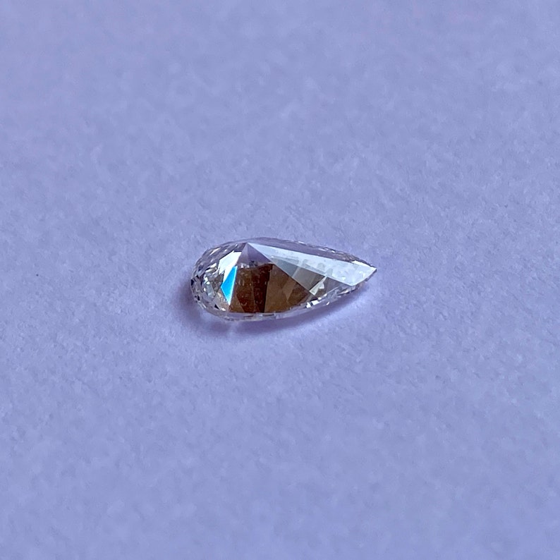 May include: A clear pear-shaped diamond gemstone on a white background.