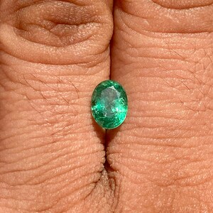 May include: A vibrant green oval emerald gemstone, showcasing its natural facets and brilliance.