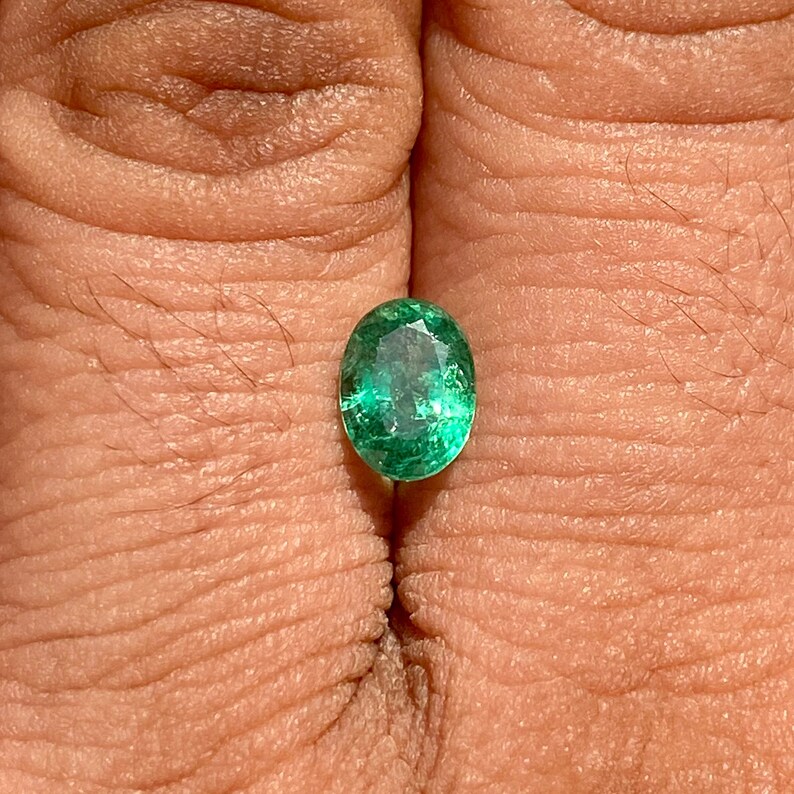 May include: A vibrant green oval emerald gemstone, showcasing its natural facets and brilliance.