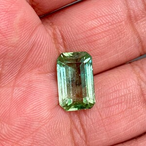 May include: A green emerald gemstone cut in an emerald shape.