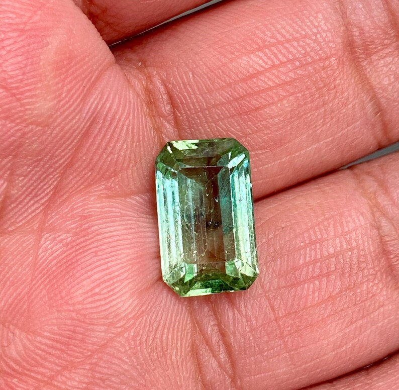 May include: A green emerald gemstone cut in an emerald shape.