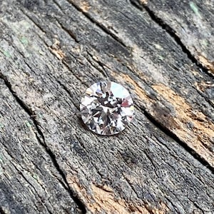 May include: A clear round diamond gemstone on a rough wooden surface.