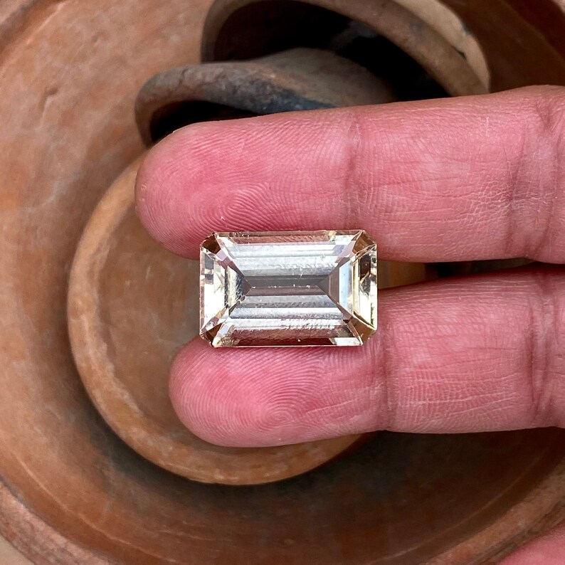 May include: A light brown, rectangular, faceted gemstone with a clear, glassy appearance.