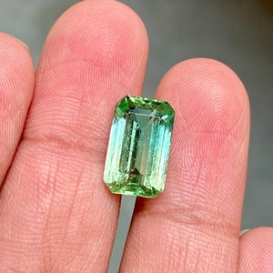 May include: A green gemstone with a light green to dark green gradient, cut in an emerald shape.