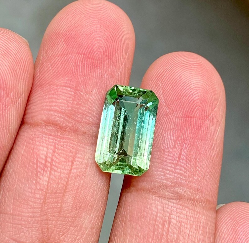 May include: A green gemstone with a light green to dark green gradient, cut in an emerald shape.