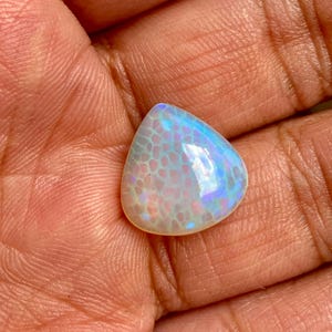 May include: A pearlescent white opal cabochon with a teardrop shape and iridescent blue and purple flashes.