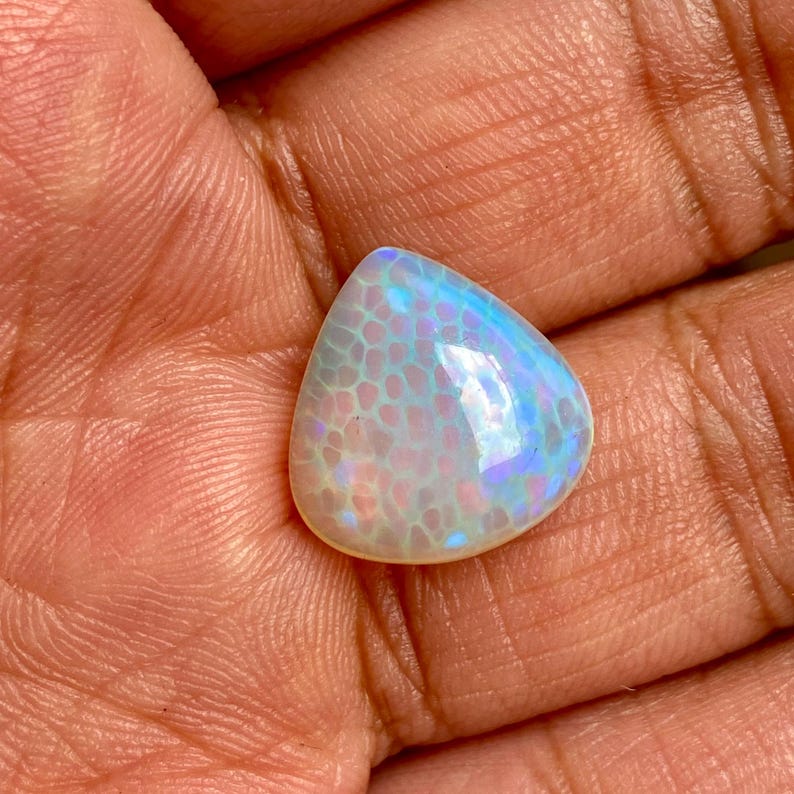 May include: A pearlescent white opal cabochon with a teardrop shape and iridescent blue and purple flashes.