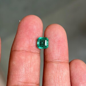 May include: A loose, square-cut emerald gemstone with a vibrant green hue and faceted surface. The stone displays internal clarity characteristics and light reflection across its polished top, showcasing a classic step-cut design with sharp corners.