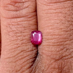Puede incluir: Una gema rosa vibrante con un corte cojín, mostrando un diseño facetado.