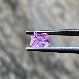 Puede incluir: Una piedra preciosa de color p&uacute;rpura claro con forma cuadrada, sostenida por unas pinzas.