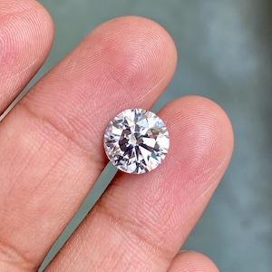 May include: A large, clear, round, faceted gemstone with a brilliant cut. The gemstone is held in a person's hand.