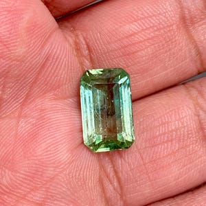 May include: A light green emerald gemstone cut in an emerald shape.
