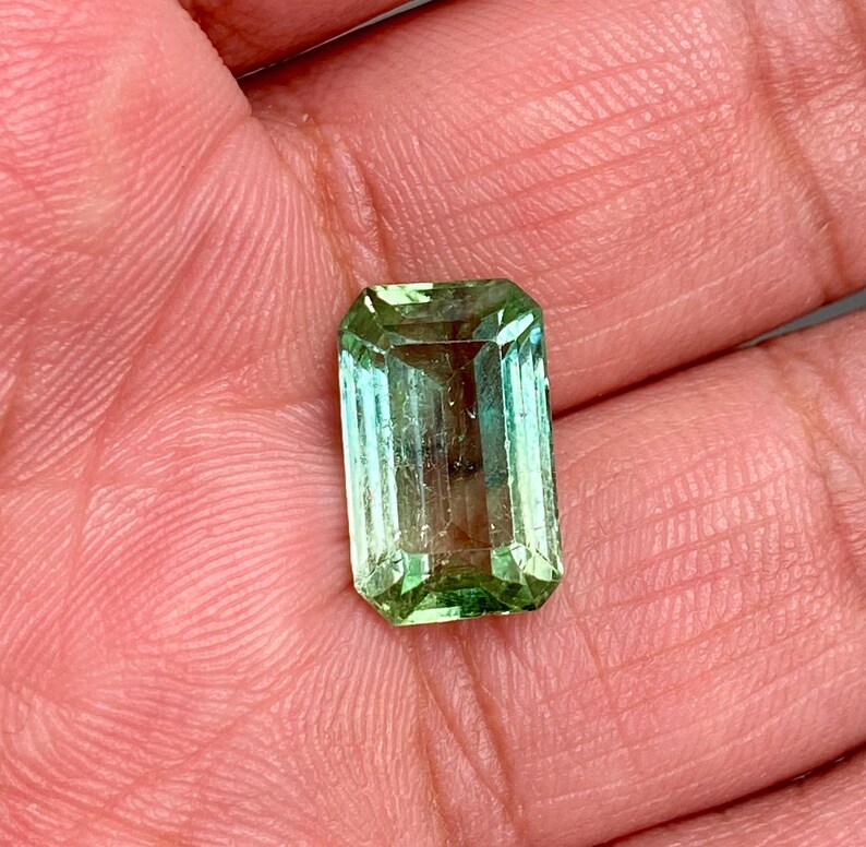 May include: A light green emerald gemstone cut in an emerald shape.