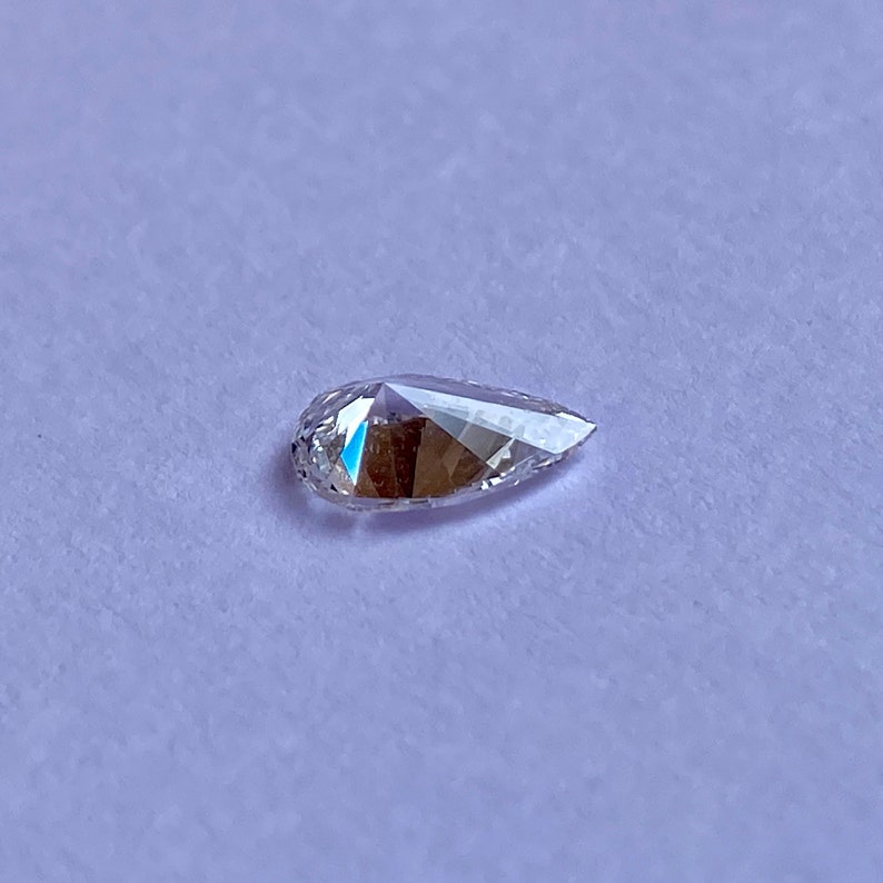 May include: A pear-shaped clear diamond gemstone on a white background.