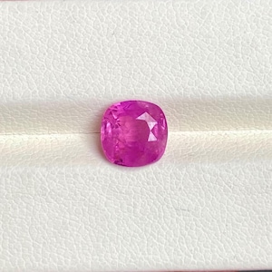 Puede incluir: Una gema rosa vibrante con un corte de cojín. La gema está colocada sobre un fondo blanco.