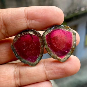 Pu&ograve; includere: Due fette di gemme rosa, verdi e marroni con un bordo grezzo e naturale. Le fette sono traslucide e hanno un aspetto stratificato.