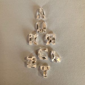 Pode incluir: Uma coleção de cristais de vidro transparente em forma de letras, formando a palavra "LUCKY".