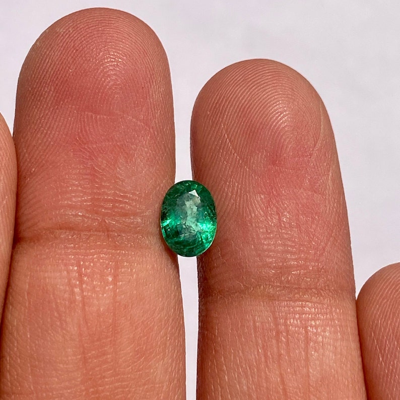 May include: A vibrant green oval emerald gemstone, showcasing its natural inclusions and facets.