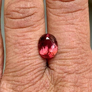 K&ouml;nnte beinhalten: Ovaler rosafarbener Edelstein mit facettiertem Schliff. Der Edelstein ist in einem Ring gefasst und wird an einem Finger getragen.