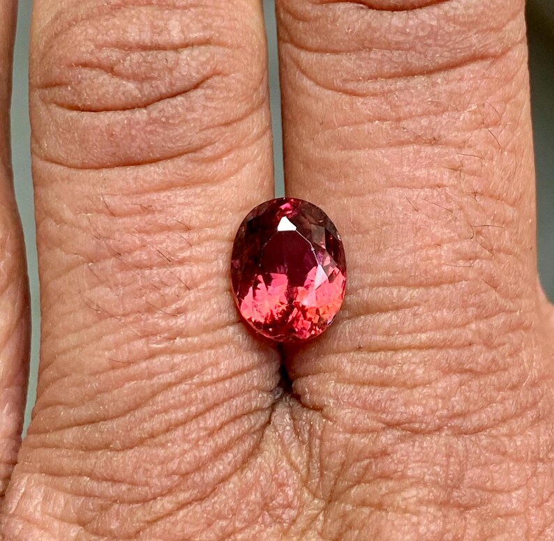 K&ouml;nnte beinhalten: Ovaler rosafarbener Edelstein mit facettiertem Schliff. Der Edelstein ist in einem Ring gefasst und wird an einem Finger getragen.