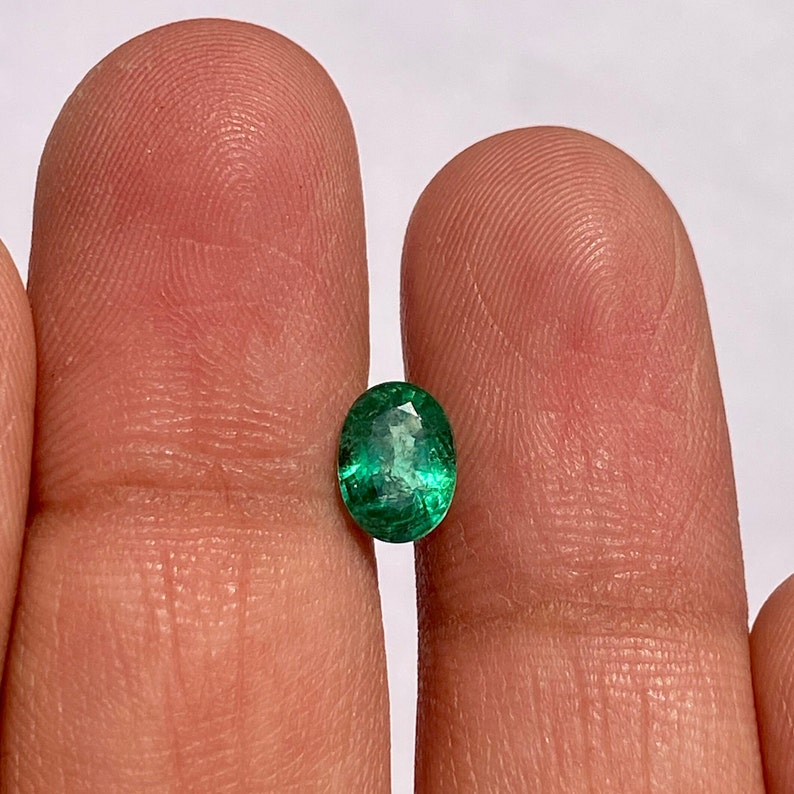 May include: A vibrant green oval emerald gemstone, showcasing its natural facets and inclusions.