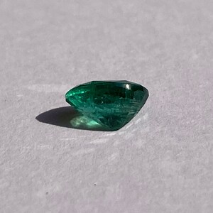 May include: A deep green emerald gemstone with a faceted cut.