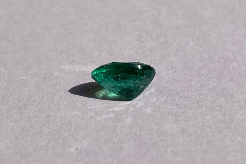 May include: A deep green emerald gemstone with a faceted cut.