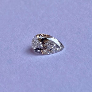 May include: A pear-shaped diamond gemstone with a clear, faceted surface.