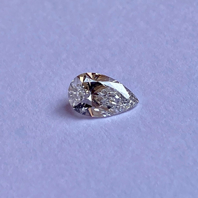 May include: A pear-shaped diamond gemstone with a clear, faceted surface.