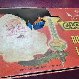 May include: A vintage Glolite Bubble-Lites cardboard box featuring a graphic of Santa Claus and a bubble light. The red box displays the text Glolite Bubble-Lites and Clip Holds Bubble-Lite Upright, with colorful light bulbs visible inside.