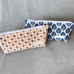 May include: Two rectangular zipped pouches with white zips. The front pouch features an orange and blue geometric circle pattern. The back pouch has a blue and cream leaf-like motif. Both pouches have a white label reading Weird Princess.