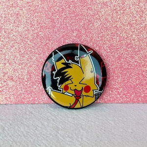 May include: A round, black button featuring a yellow cartoon character with a red tie and red cheeks. The character is smiling and has black hair. The button has a glossy finish and is set against a pink background.