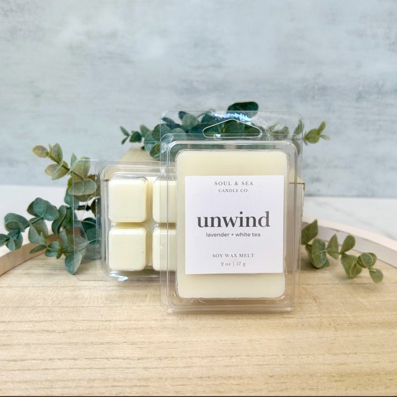 Puede incluir: Un derretido de cera de soja blanco en un recipiente de pl&aacute;stico transparente con el texto "SOUL & SEA CANDLE CO unwind lavender + white tea SOY WAX MELT 2 oz | 57 g"