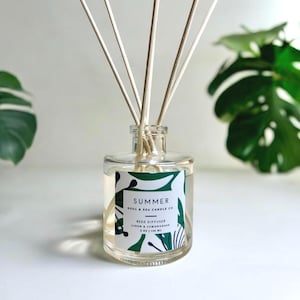 May include: A clear glass reed diffuser bottle with a label reading SUMMER SOUL & SEA CANDLE CO. REED DIFFUSER LINEN & LEMONGRASS 5 OZ | 148 ML. The label features a green and white botanical pattern. Several light-colored wooden reeds extend upward.